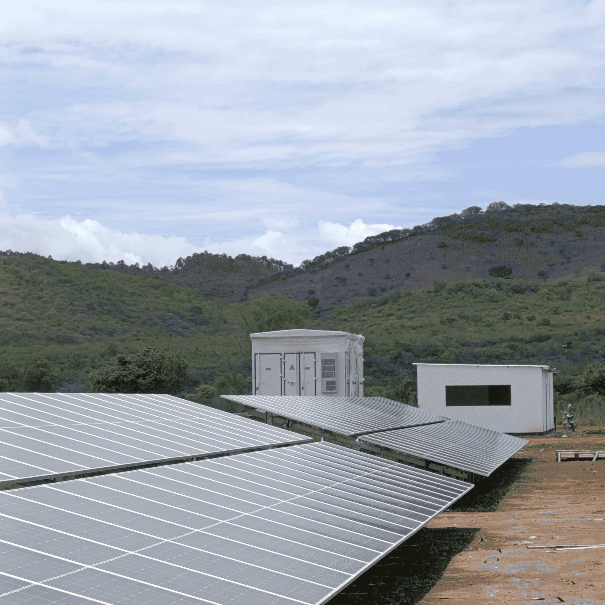 Paneles solares junto a dos construcciones prefabricadas, una de ellas rotulada A2, con colinas verdes al fondo